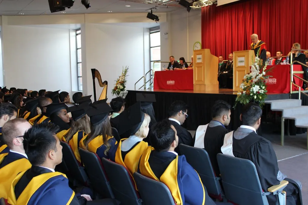 Several rows of graduates in cap & gowns look up at a raised dais with a speaker at a Griffith College graduation ceremony